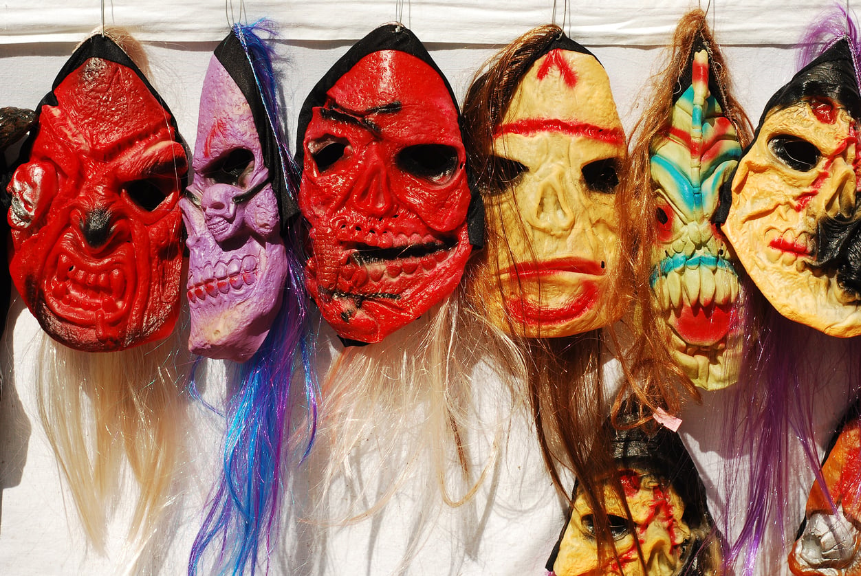 A row of colorful plastic Halloween masks with long synthetic hair, hanging against a white background. Halloween in the 1970s.