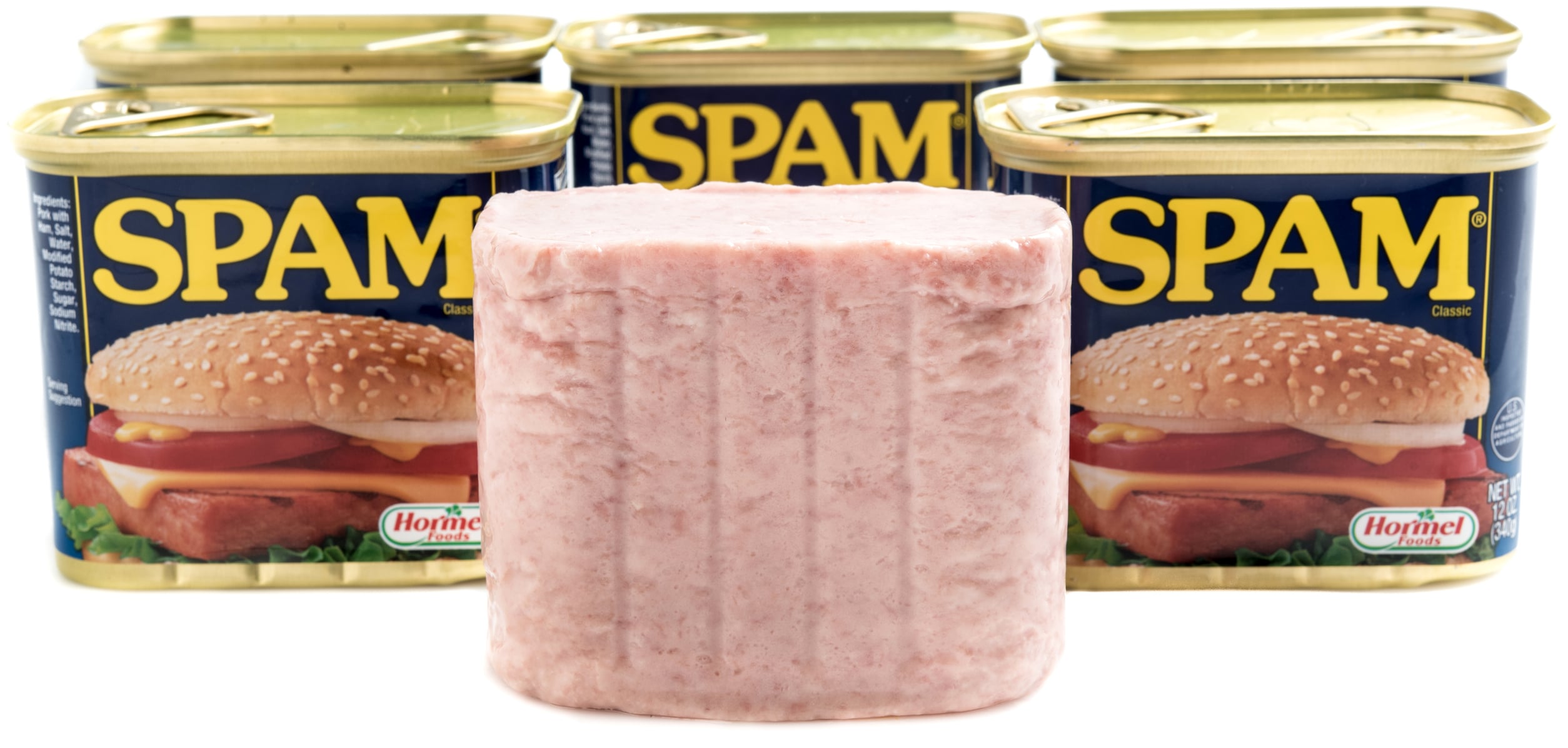 A block of luncheon meat standing in front of three cans of Spam.