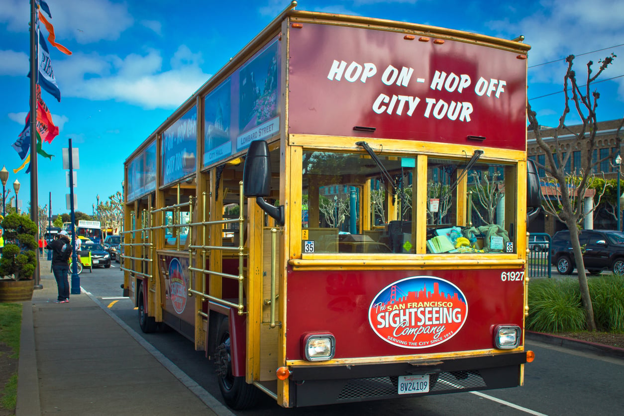 A red, open-top San Francisco Sightseeing Company tour bus parked on a city street.