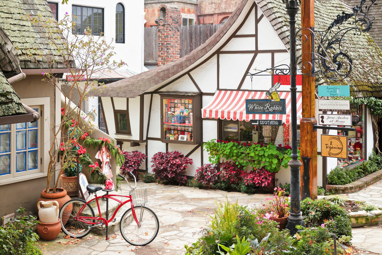 A red bicycle sits in a courtyard surrounded by half-timbered shops with signs for “White Rabbit” and other businesses.