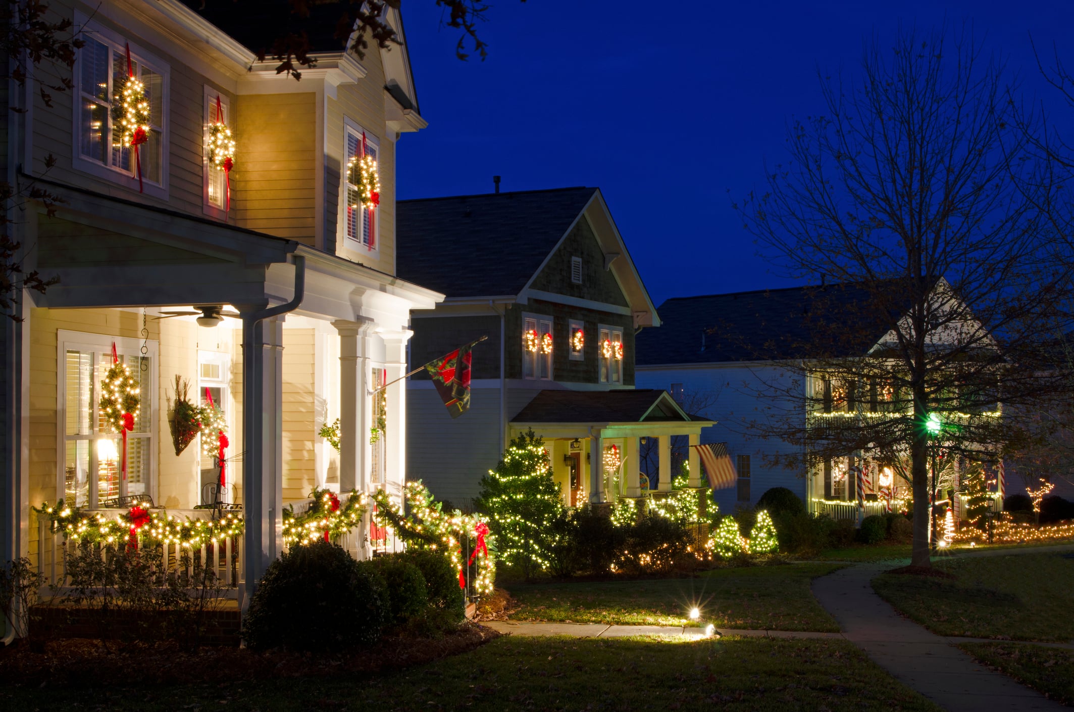 Suburban houses decorated with Christmas lights at dusk, featuring wreaths on windows and glowing garlands on front porches.