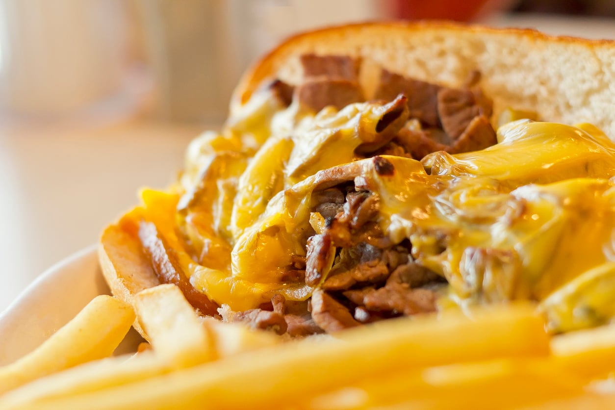 A cheesesteak sandwich topped with melted cheese, served with a side of french fries.