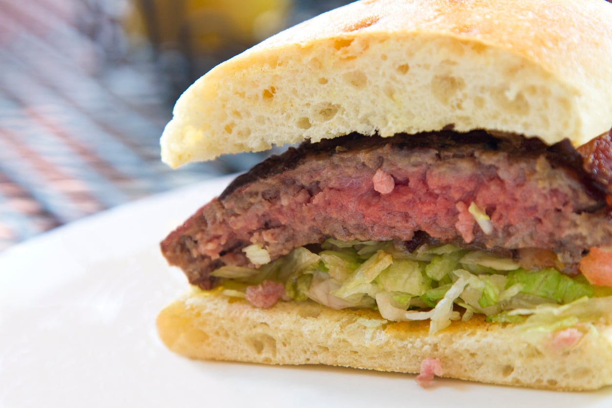 A close-up of a medium-rare burger patty topped with shredded lettuce on a toasted bun, a classic choice for restaurant menus.