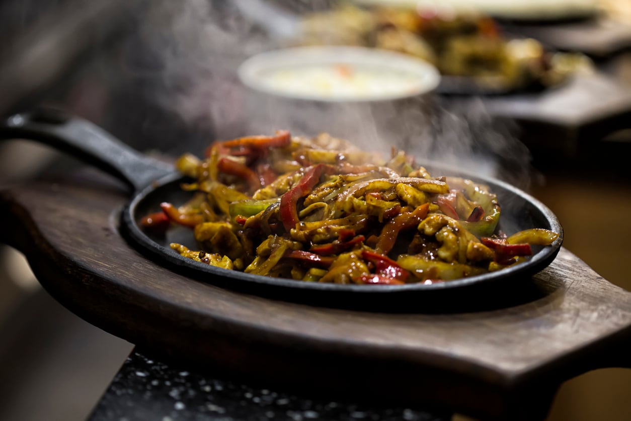 Steaming chicken fajitas with sliced peppers and onions served on a hot cast-iron skillet.