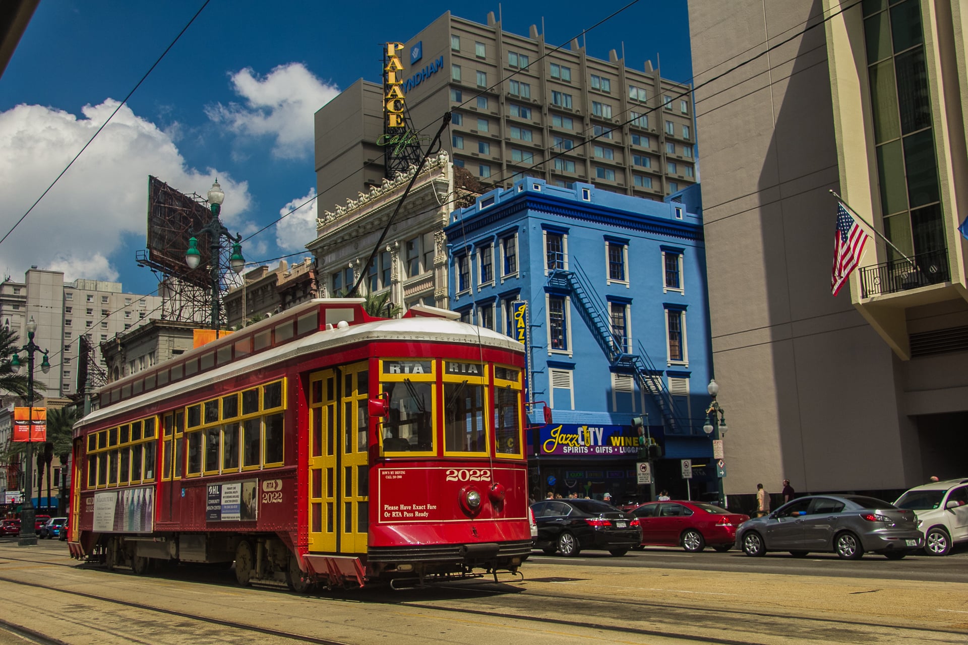 A red and yellow RTA streetcar travels down a street in New Orleans, passing a bright blue building and the Palace Cafe.