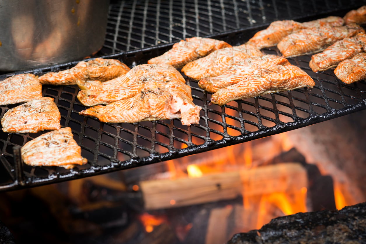 Salmon fillets grilling on a metal grate over an open fire.