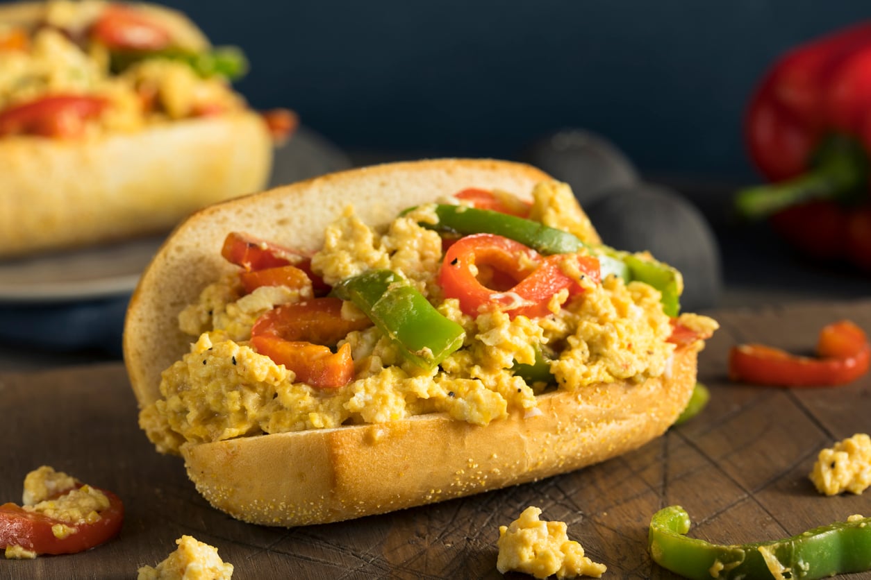 A breakfast sandwich on a roll filled with scrambled eggs, red peppers, and green peppers.