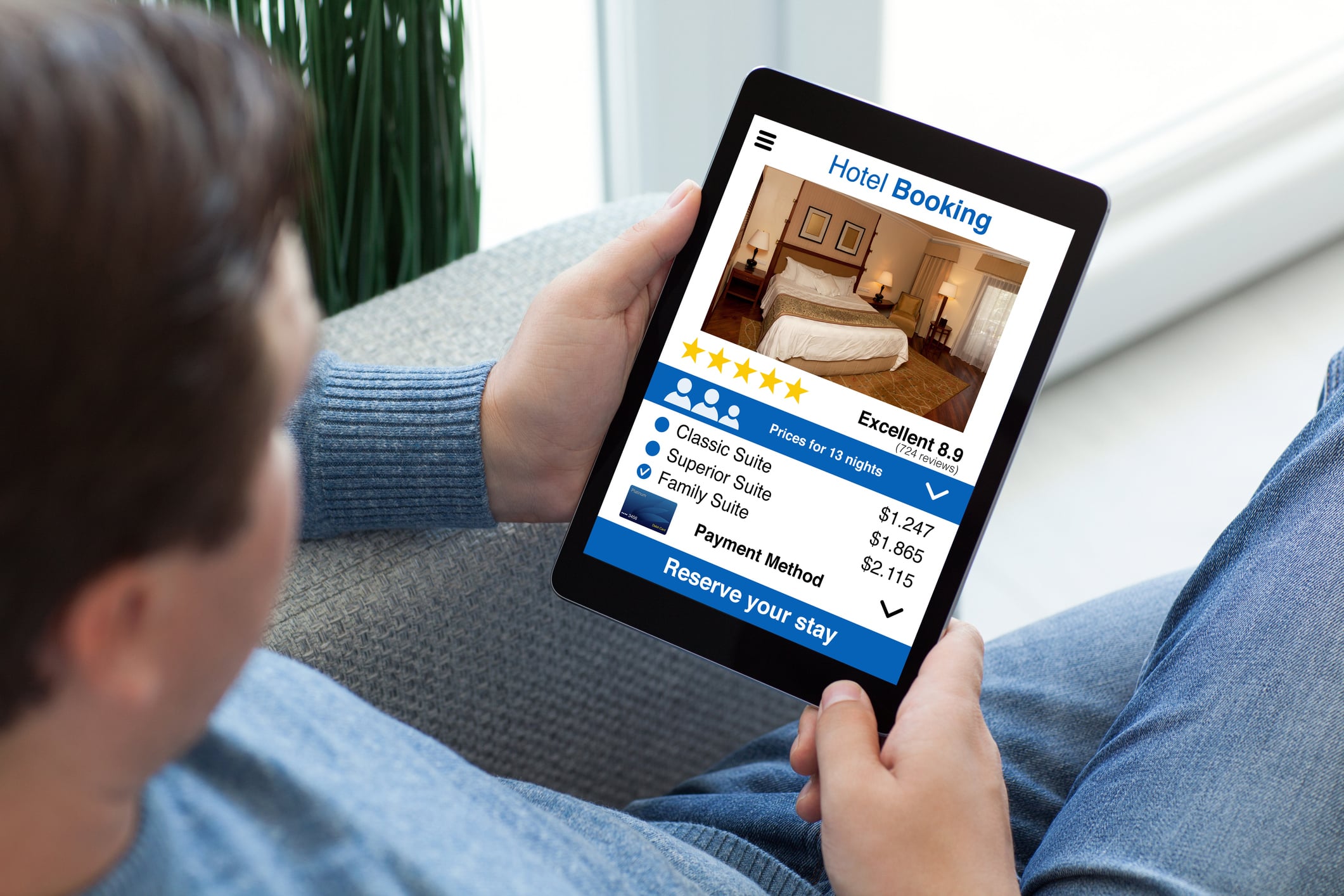 A person holding a tablet displaying a hotel booking app with room options, prices, and a reserve button.