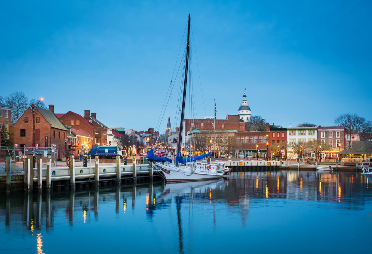 A sailboat docked along the waterfront in Annapolis, Maryland, with historic brick buildings and the Maryland State House at dusk—one of those American Destinations That Feel Bigger than their charming size suggests.
