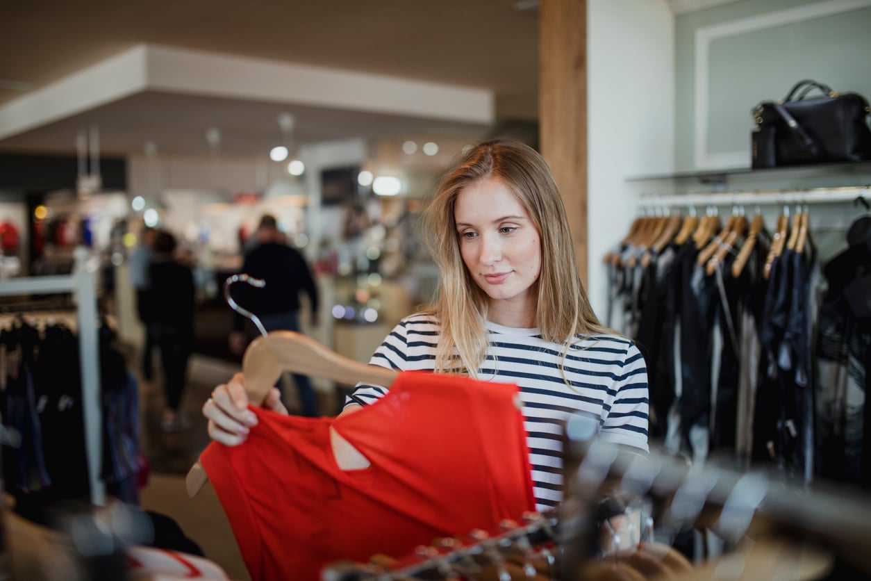 A woman in a striped shirt holding a red garment while shopping in a clothing store.