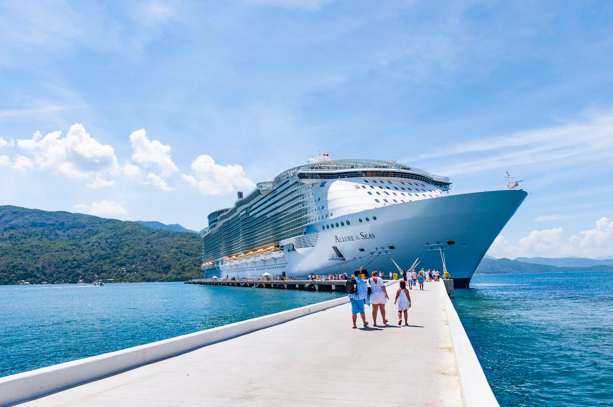 The Allure of the Seas cruise ship docked at a pier with tourists walking toward the vessel.