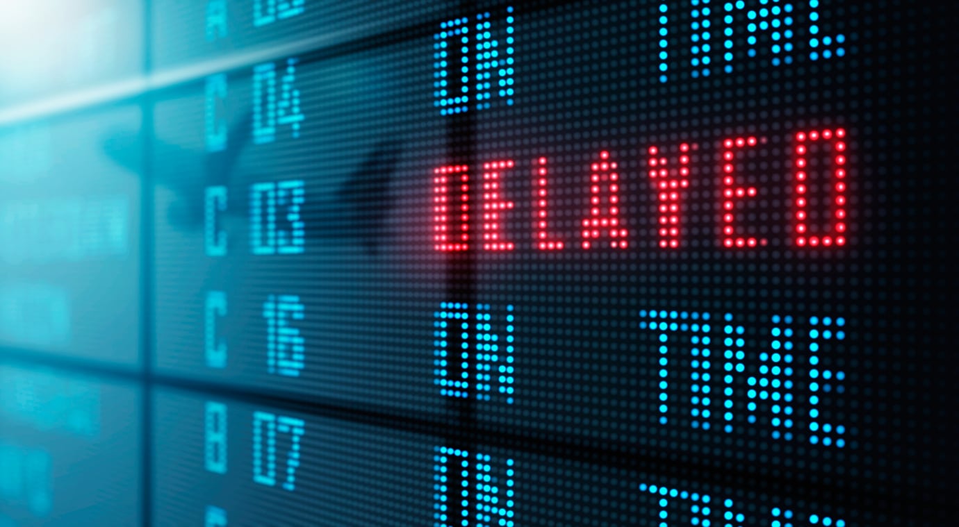 An airport digital flight information display showing one flight status as “DELAYED” in red text and others as “ON TIME” in blue text.