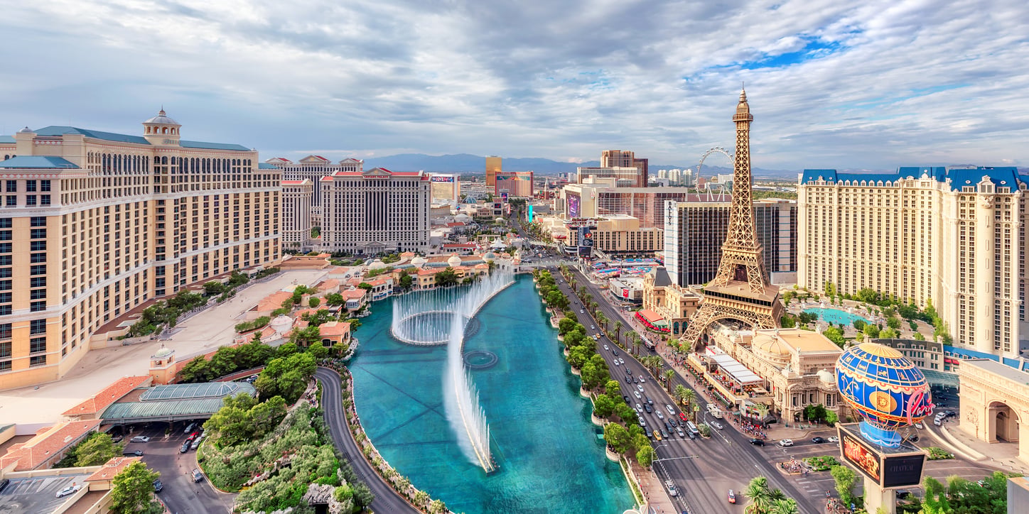 Aerial view of the Las Vegas Strip featuring the Bellagio fountains, the Paris Las Vegas Eiffel Tower replica, and surrounding hotels.