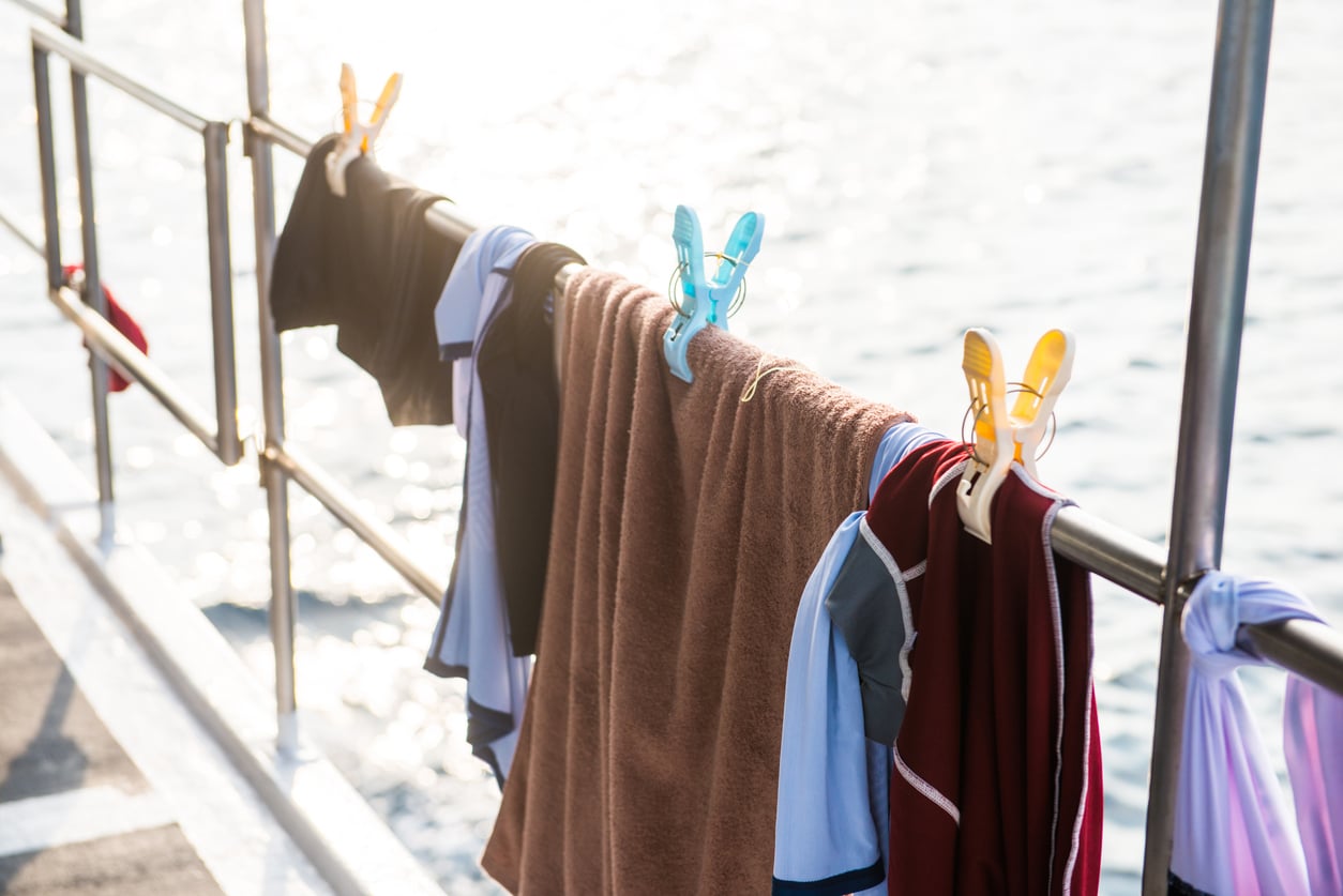 Clothing and a brown towel hanging from a metal railing over water, secured by plastic clothespins.