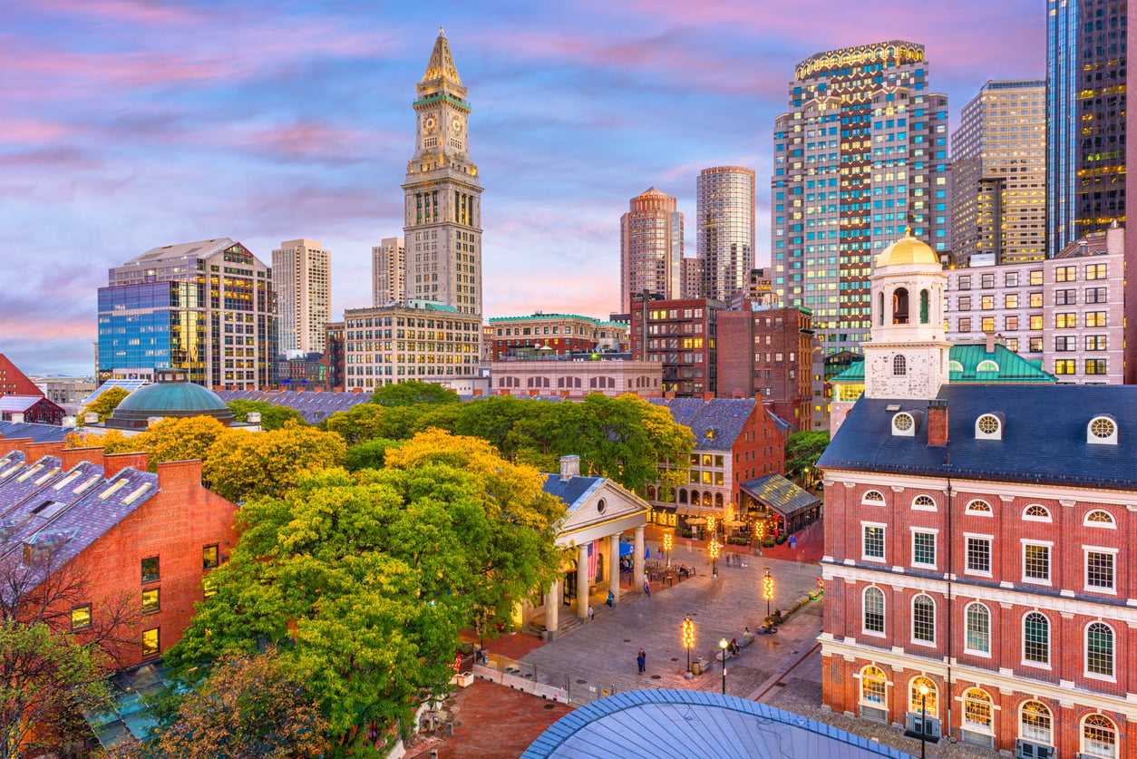 View of Faneuil Hall and the Boston skyline at sunset with yellow-leafed trees in the foreground.