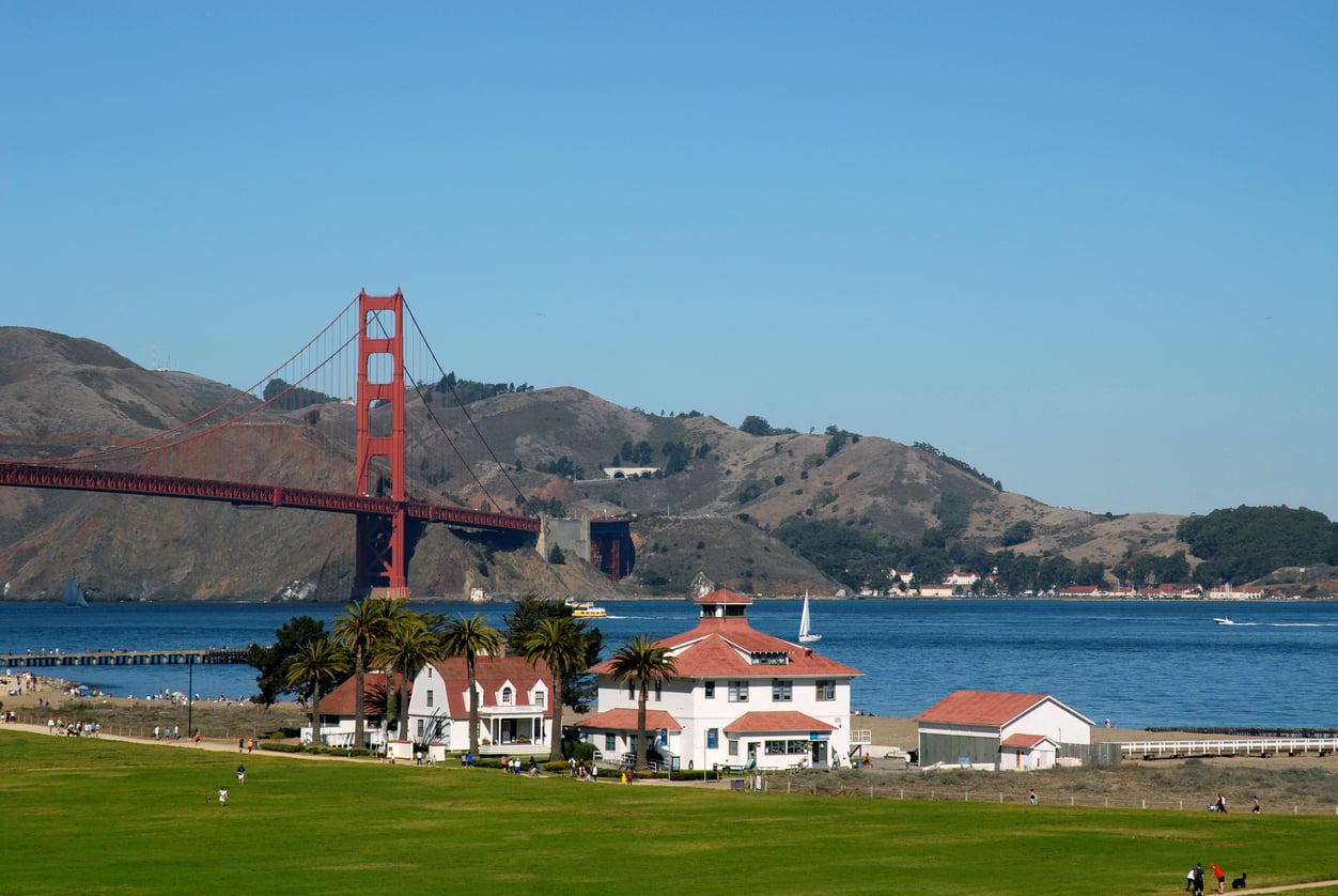 Golden Gate Bridge looming over the waterfront buildings at Crissy Field with green grass in the foreground.