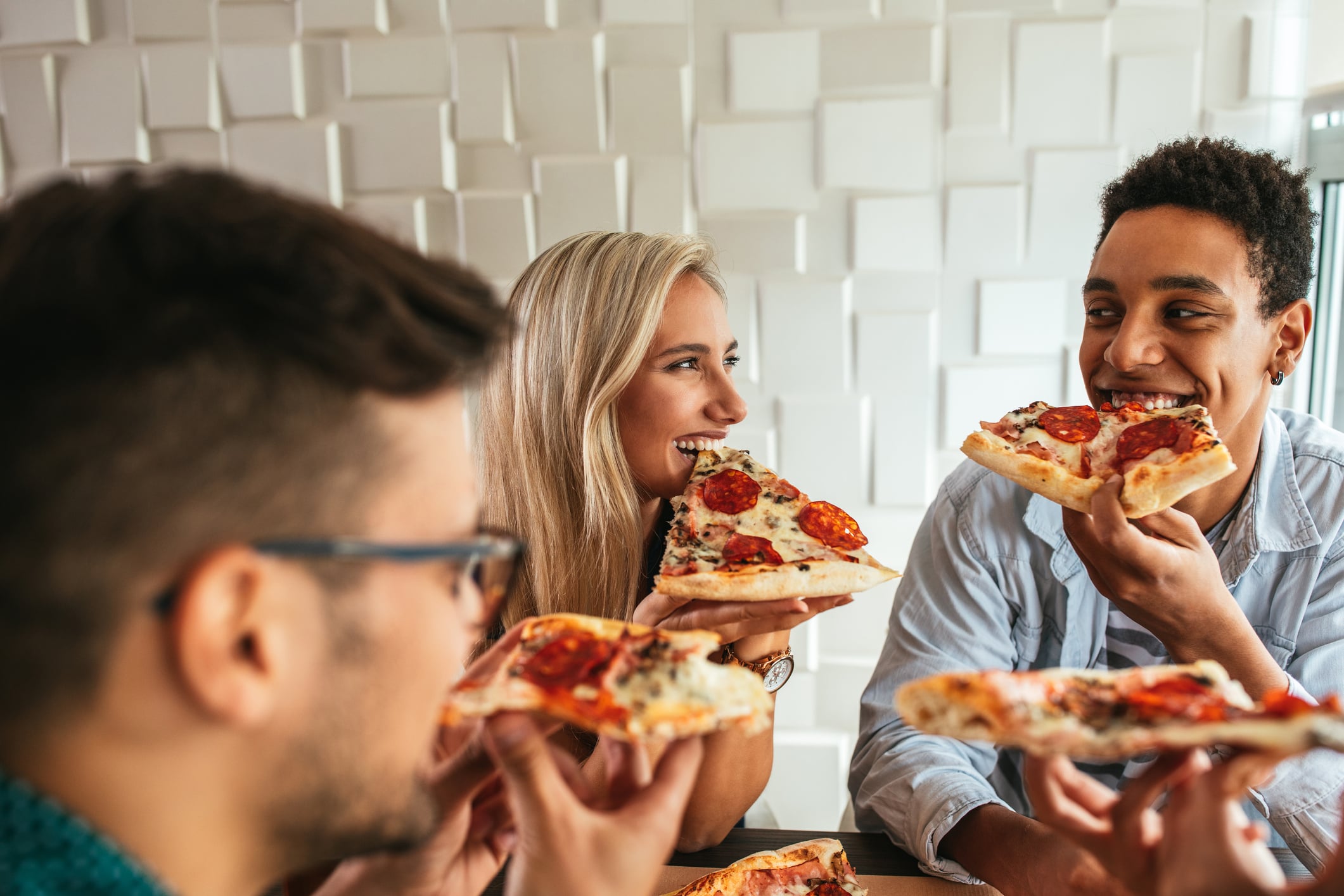 Three friends eating breakfast slices of pepperoni pizza at a table.
