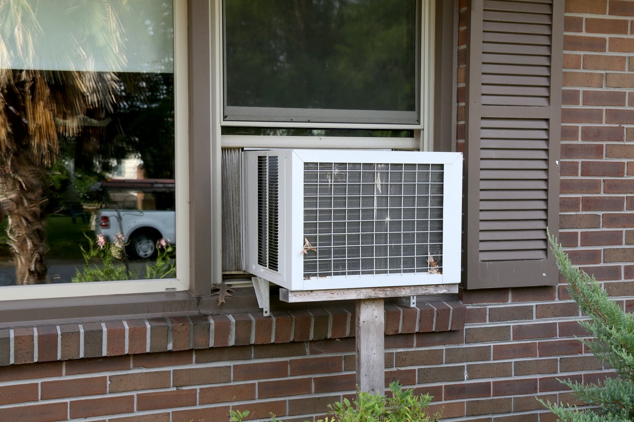 A white window air conditioning unit installed in a brick house.