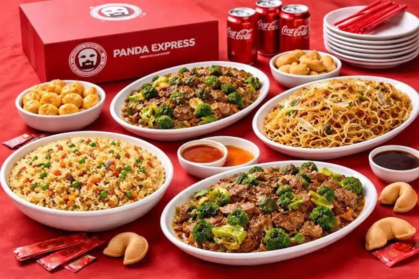 Panda Express takeout meal featuring bowls of fried rice, chow mein, and broccoli beef, with egg rolls, dipping sauces, cans of soda, and a stack of plates.