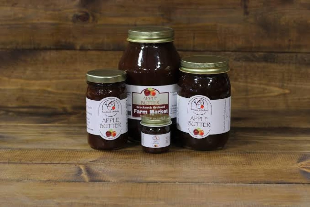 Three glass jars of Brecknock Farm Market apple butter in different sizes arranged on a wooden surface, serving as the best souvenir.