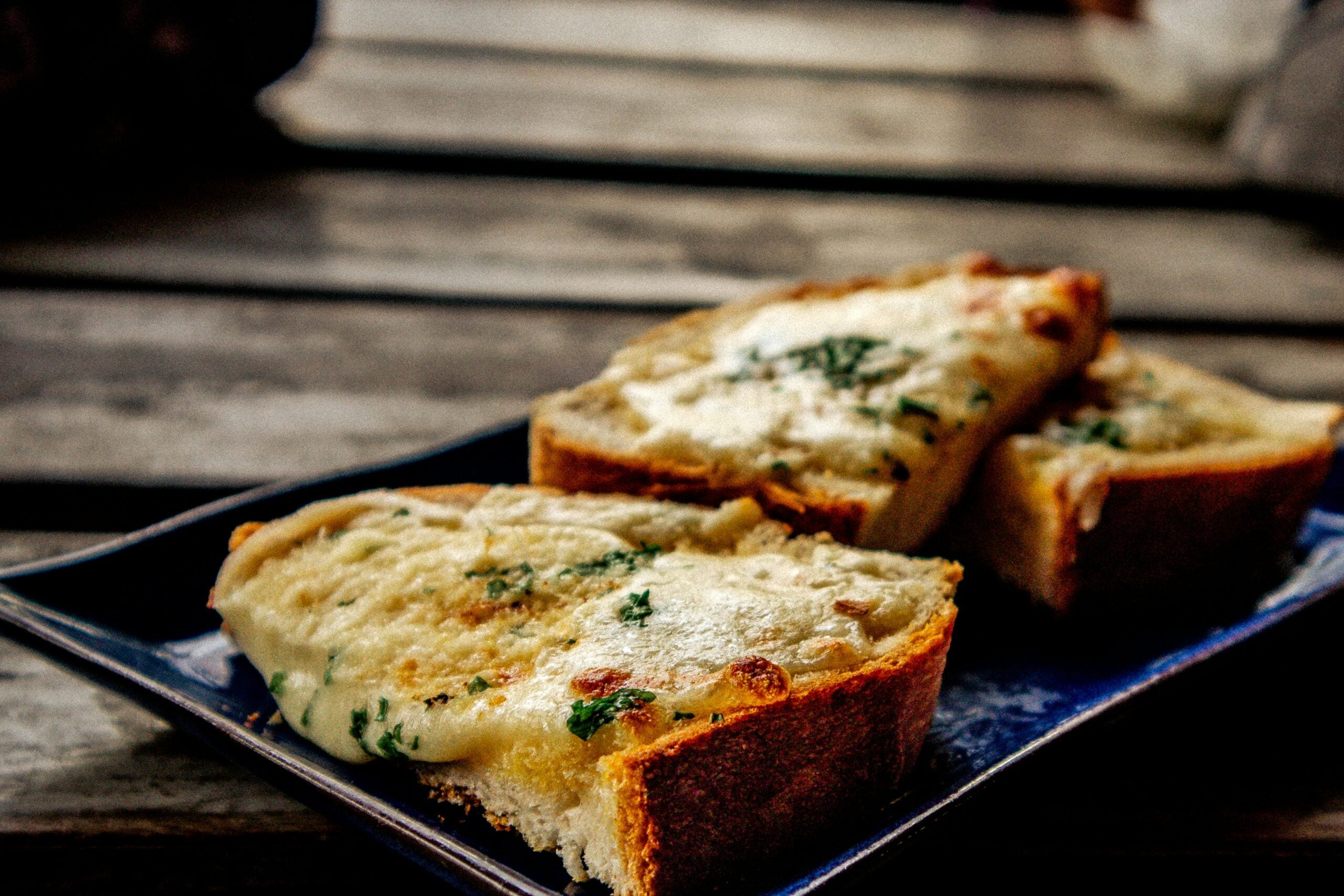 Three slices of toasted bread topped with melted cheese and herbs on a blue plate.