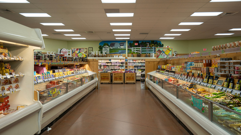 Aisle view of the refrigerated section in a grocery store, with glass-front cases stocked with various packaged food items.