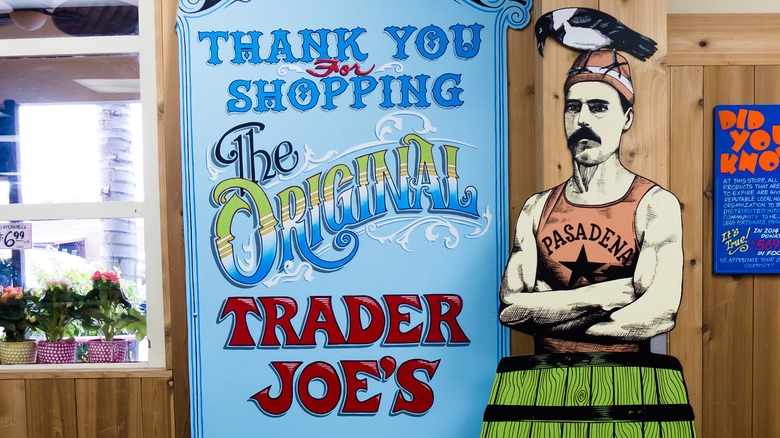 Sign reading “Thank You For Shopping The Original Trader Joe’s” next to a cartoon man with a mustache, wearing a Pasadena tank top and a bird on his head.