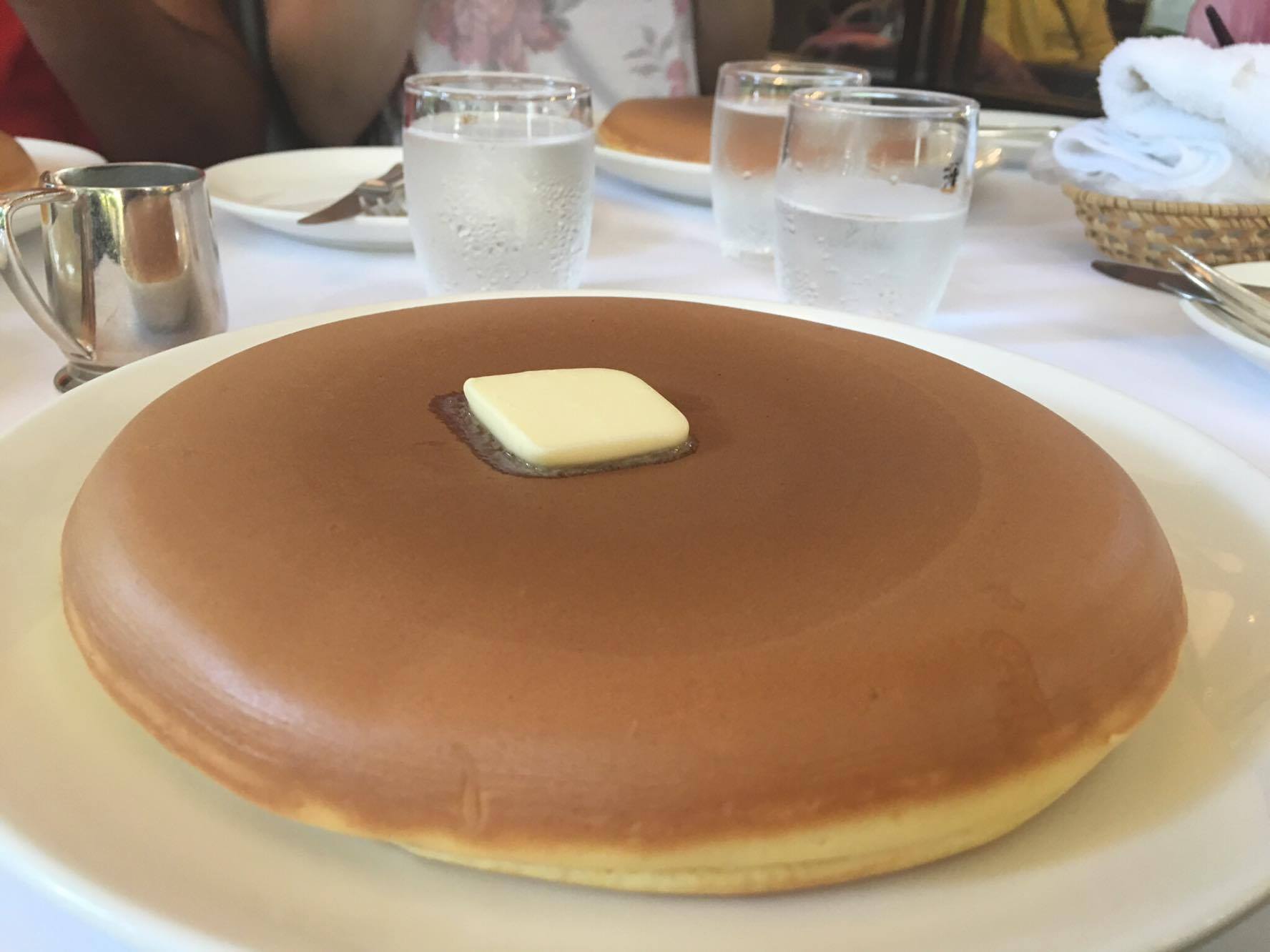 A large, thick, golden-brown pancake topped with a square pat of melting butter on a white plate.