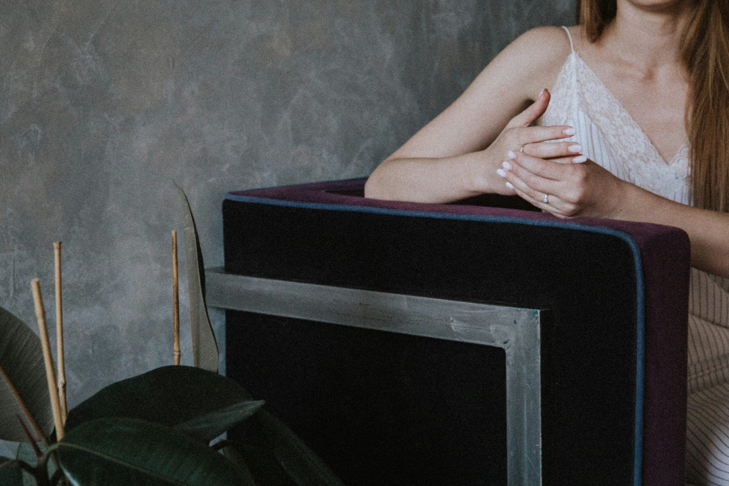 A woman with her hands clasped, resting on the arm of a dark, modern armchair.