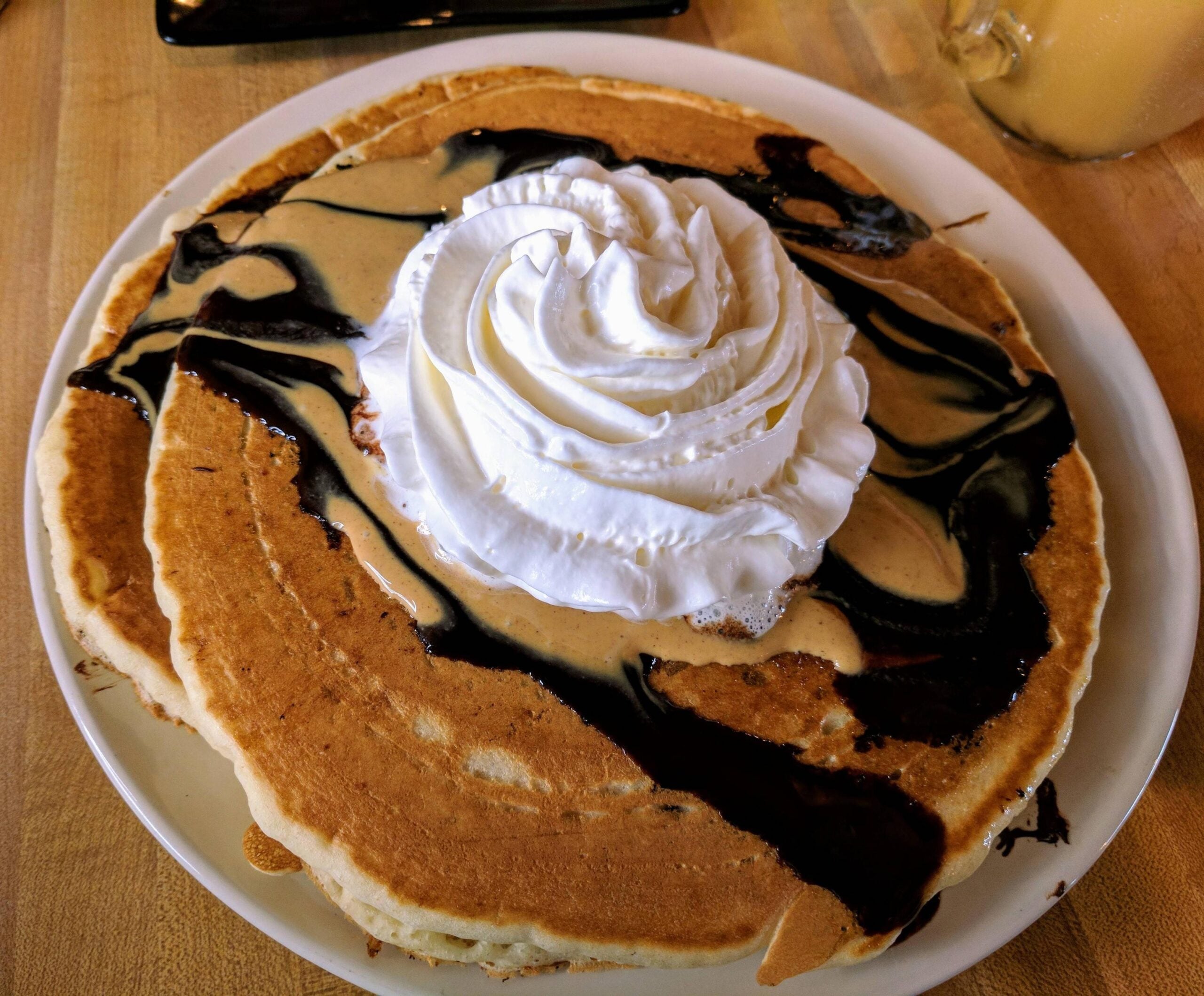 Two pancakes topped with peanut butter, chocolate sauce, and a large swirl of whipped cream.