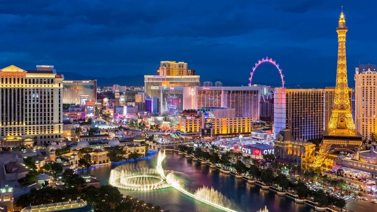 The Las Vegas Strip at night, featuring the Bellagio fountains in the foreground, the Eiffel Tower replica, and various illuminated casino resorts.