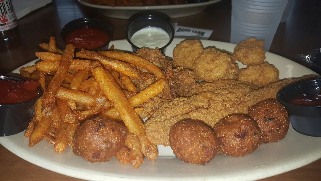 A platter of fried fish, french fries, and hushpuppies served with three small cups of dipping sauce.