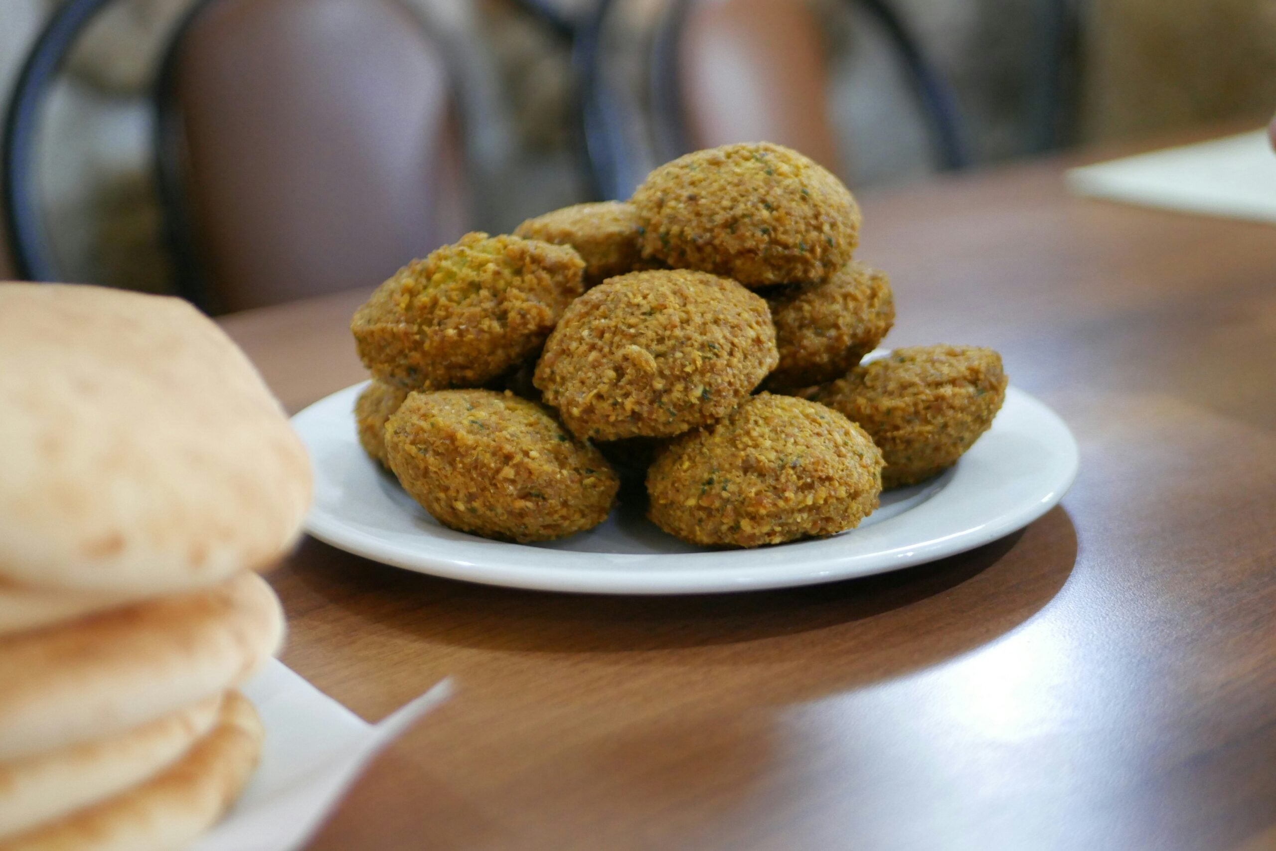 A plate of fried falafel balls next to a stack of pita bread on a wooden table.