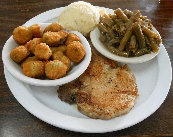 A pork chop served with a bowl of fried okra, a scoop of mashed potatoes, and a side of green beans.