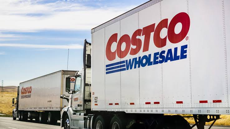 Two white semi-trucks with the Costco Wholesale logo driving along a road.