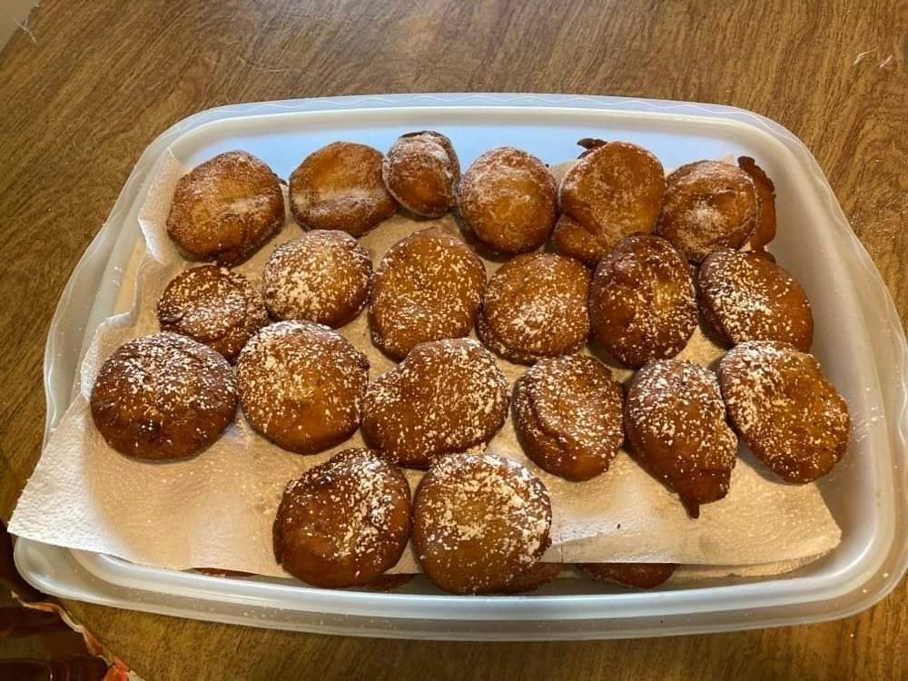 A plastic tray lined with paper towels filled with fried dough balls dusted with powdered sugar.