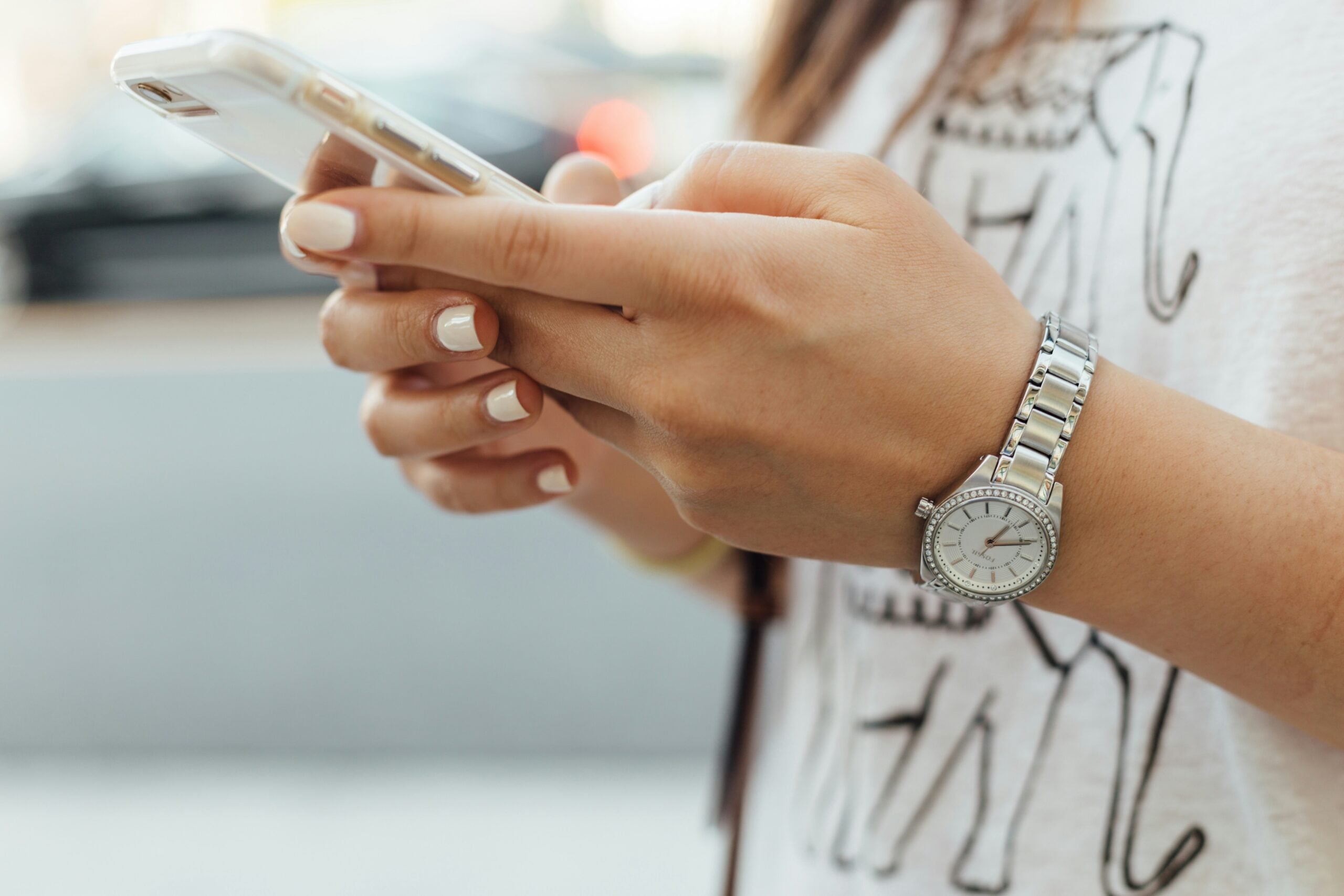 A person holding a smartphone with both hands, wearing a silver watch on their wrist.