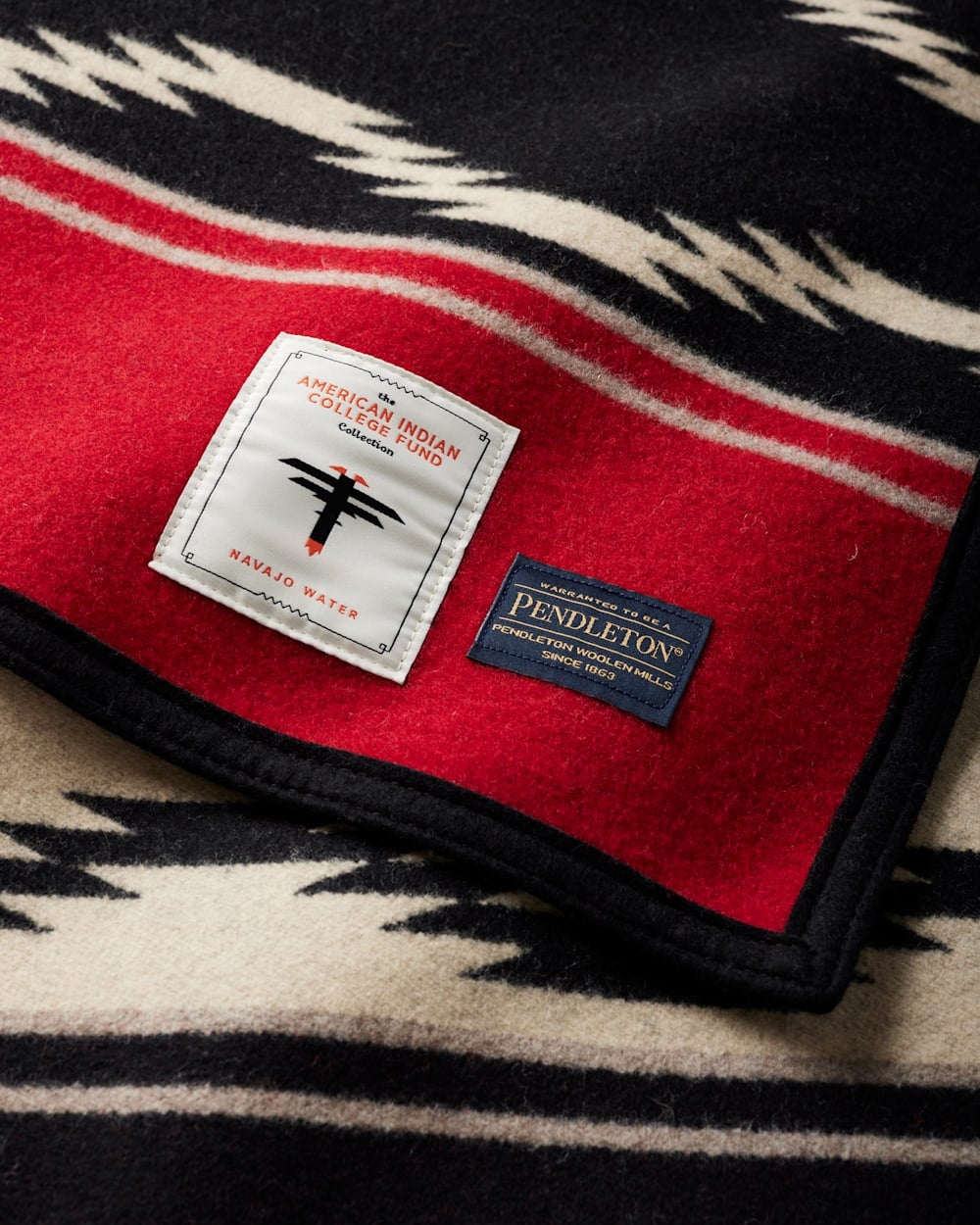 A black, white, and red patterned wool blanket with two labels: one for the American Indian College Fund Navajo Water collection and one for Pendleton.