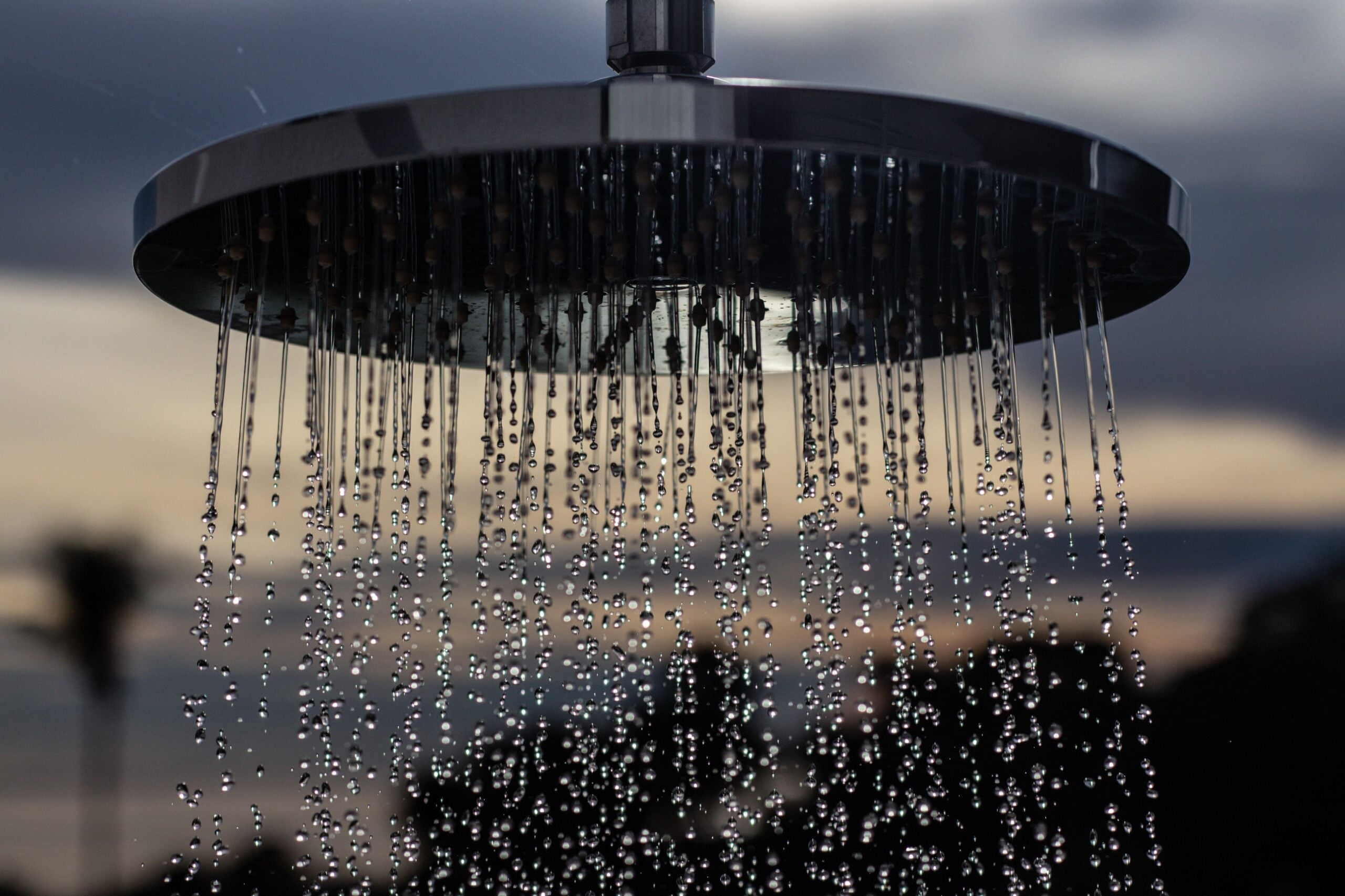A circular shower head pouring water against a blurred outdoor background.