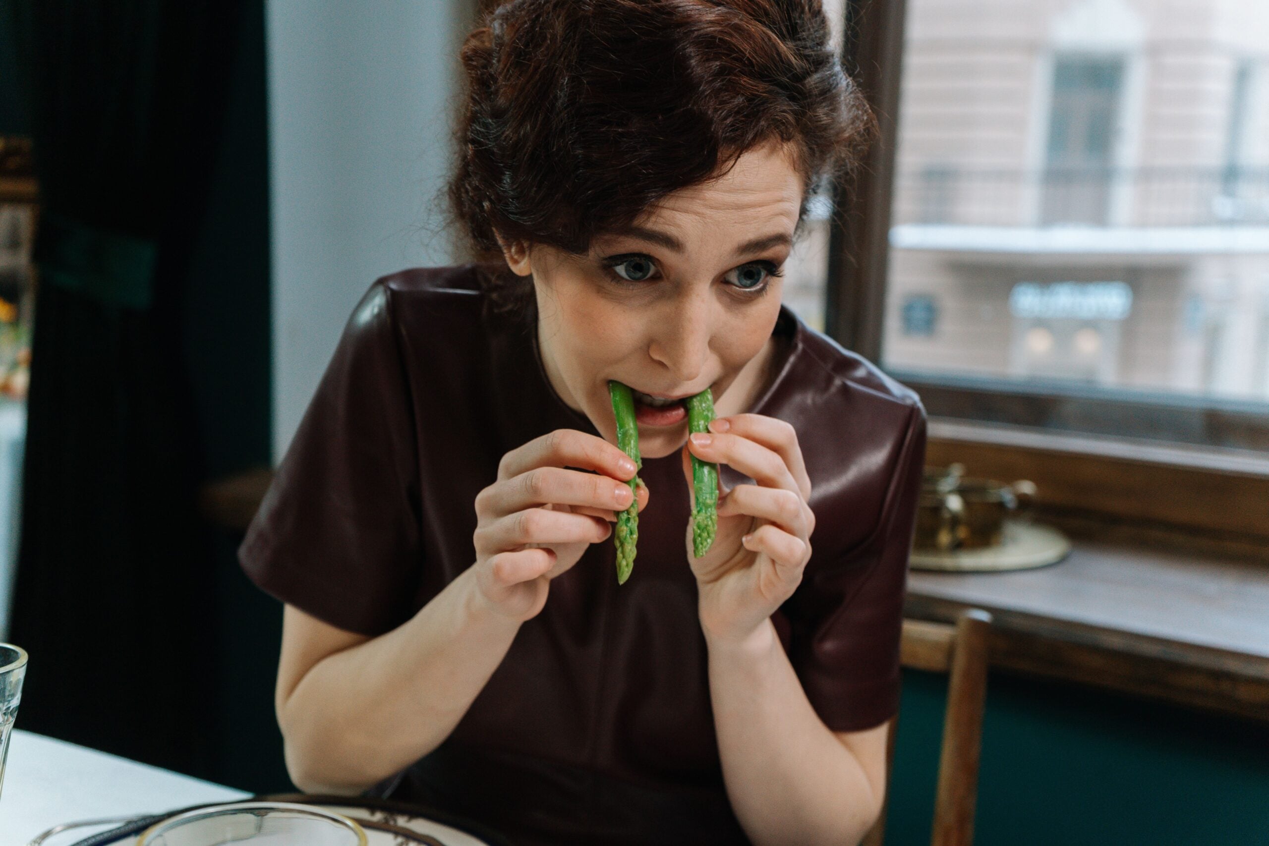 A woman holding two stalks of asparagus to her mouth.