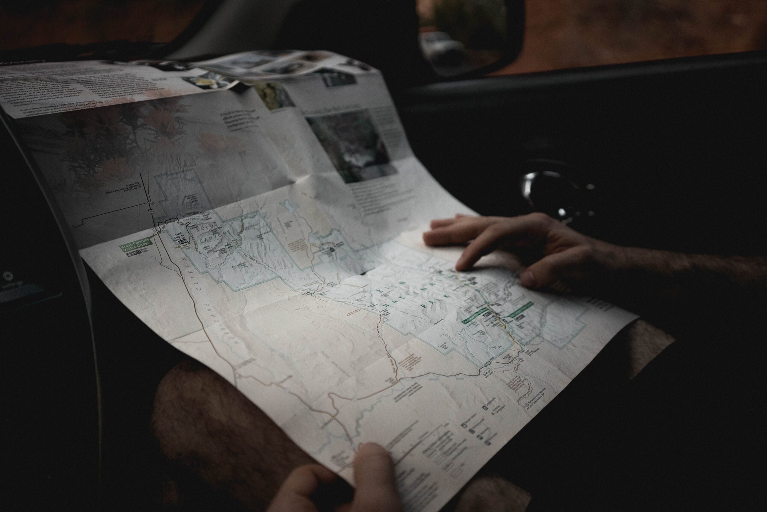 A person holds and navigates a paper map of Zion National Park inside a vehicle.