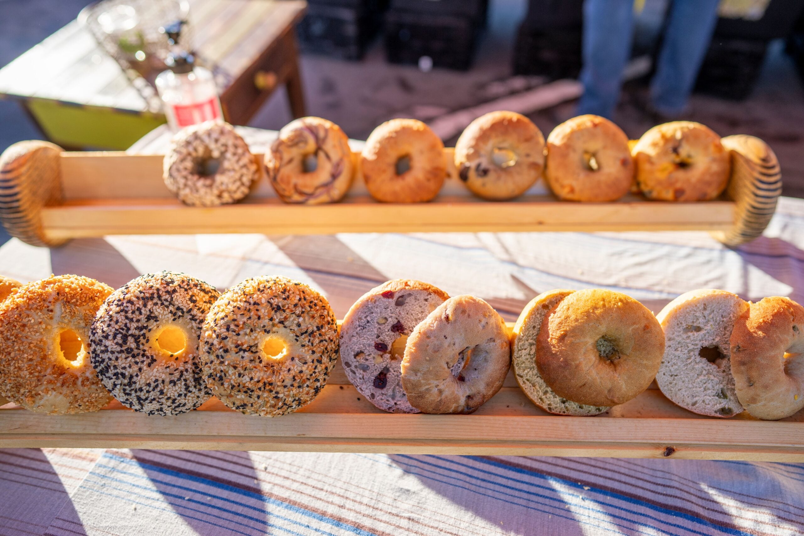 A variety of bagels displayed on two wooden shelves atop a striped tablecloth.