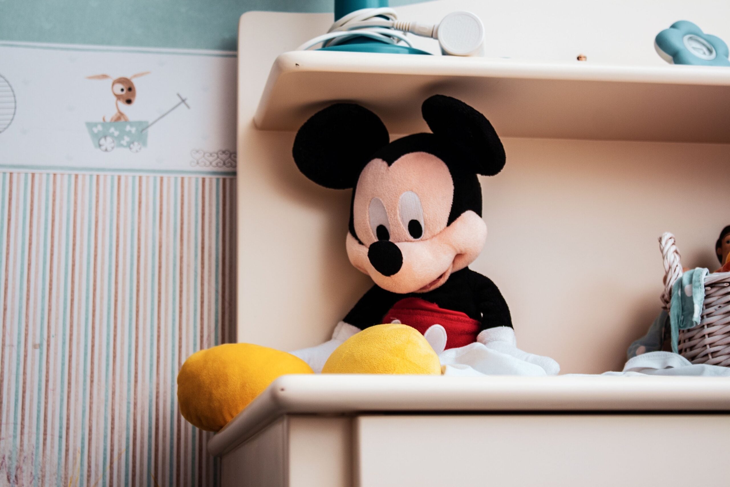 A Mickey Mouse plush toy sits on a shelf next to a small wicker basket, evoking the charm of cruise entertainment.