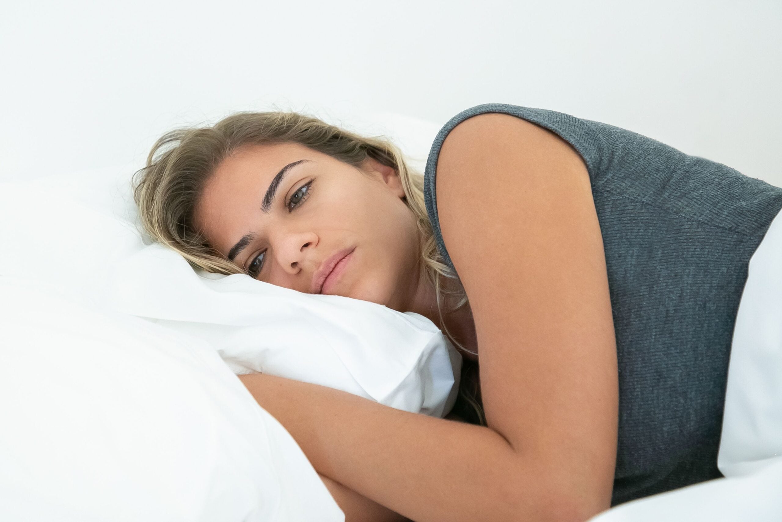 A woman lying in bed, resting her head on a white pillow and looking toward the camera.