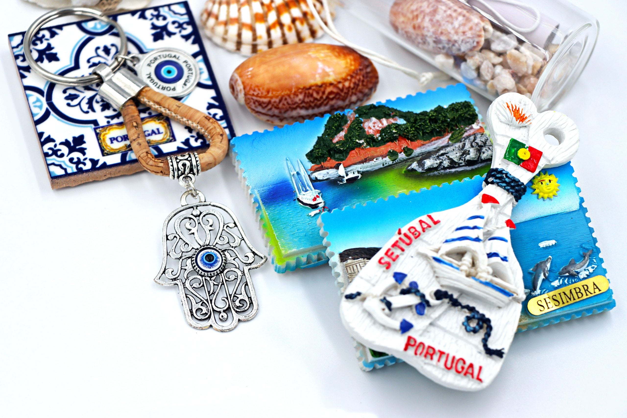Assorted Portugal souvenirs including magnets, a keychain with a hamsa hand, shells, and beach-themed items arranged on a white surface.