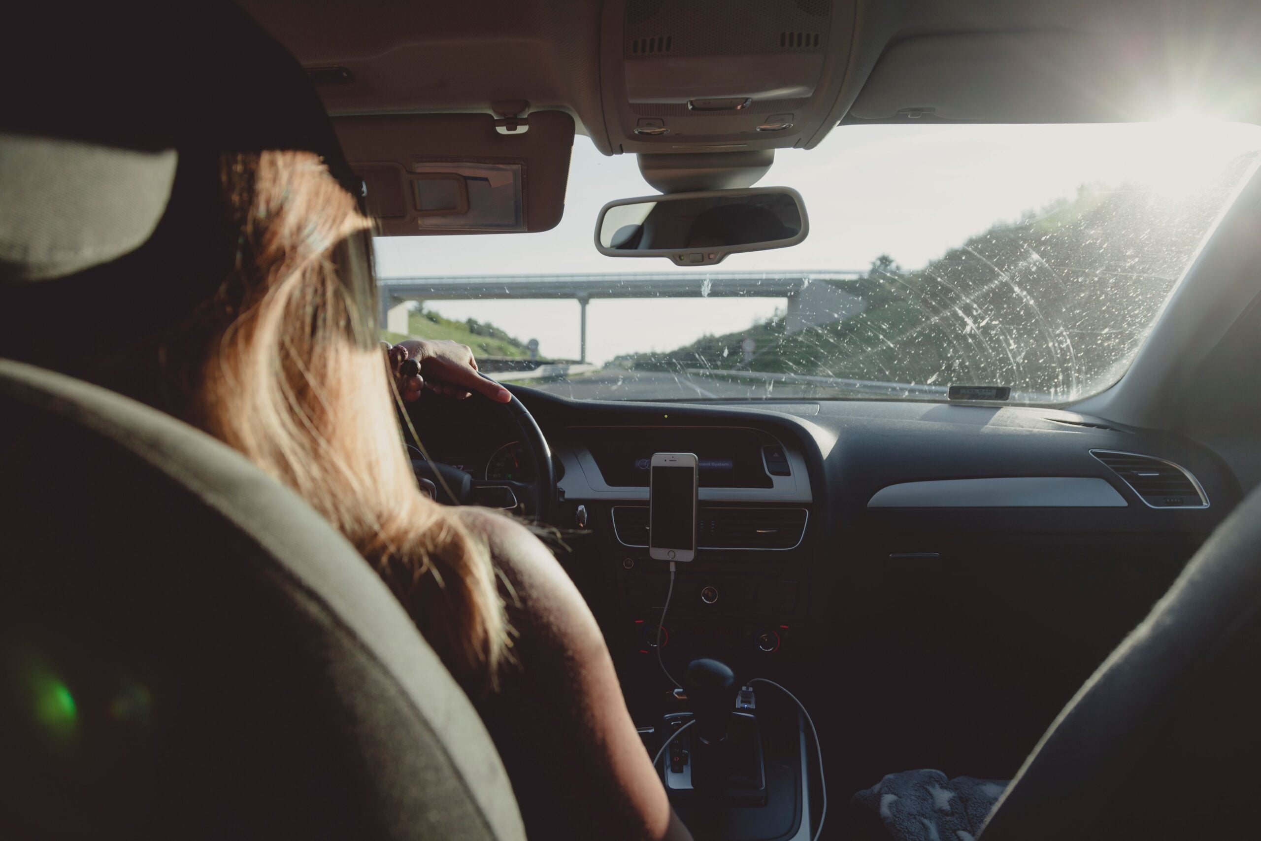 A person driving a car with a smartphone mounted on the dashboard.