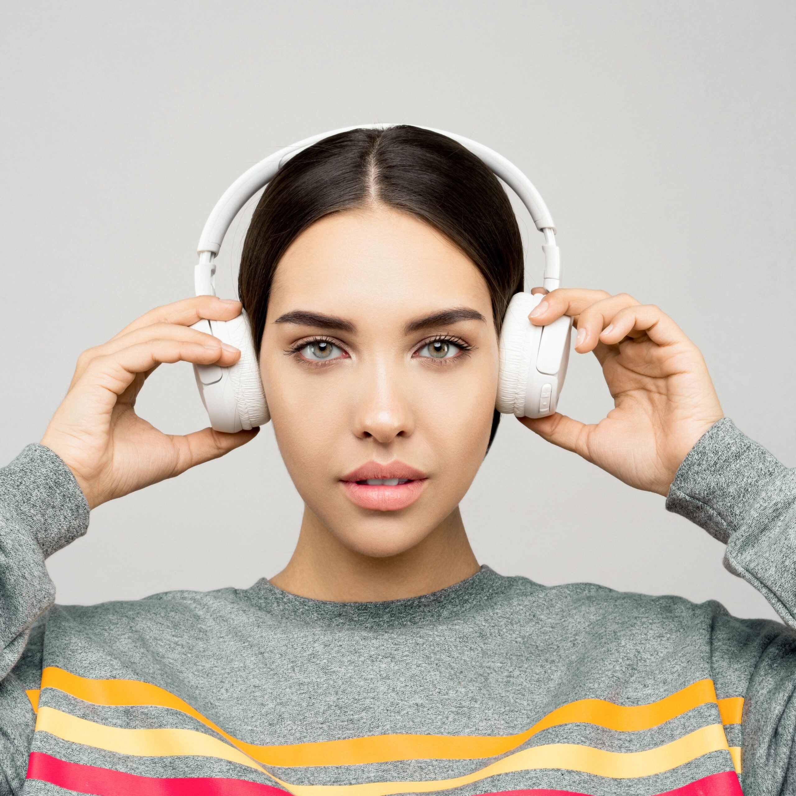 A person wearing white over-ear headphones, holding the ear cups with both hands.
