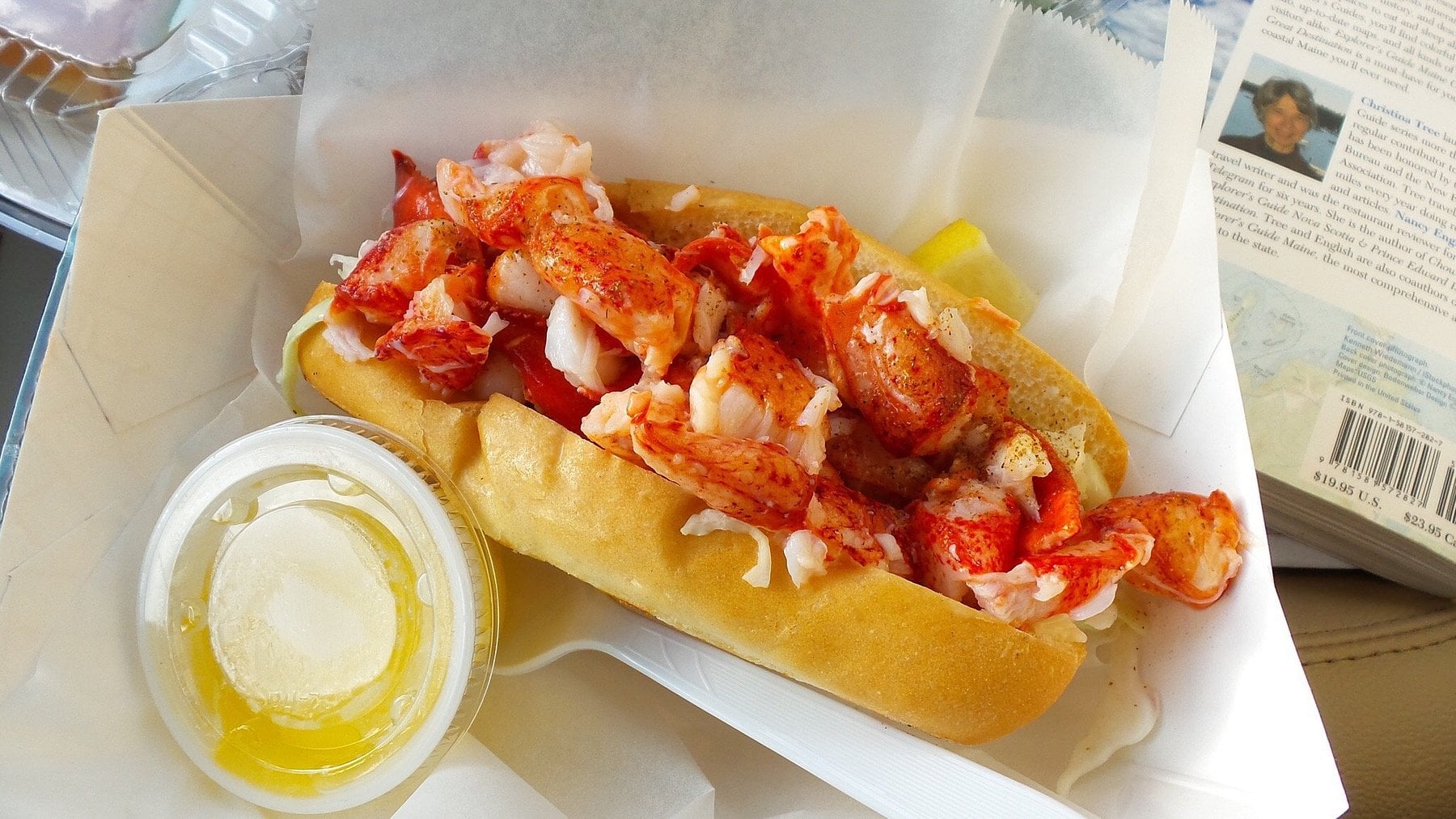 A lobster roll served in a paper container with a side of melted butter.
