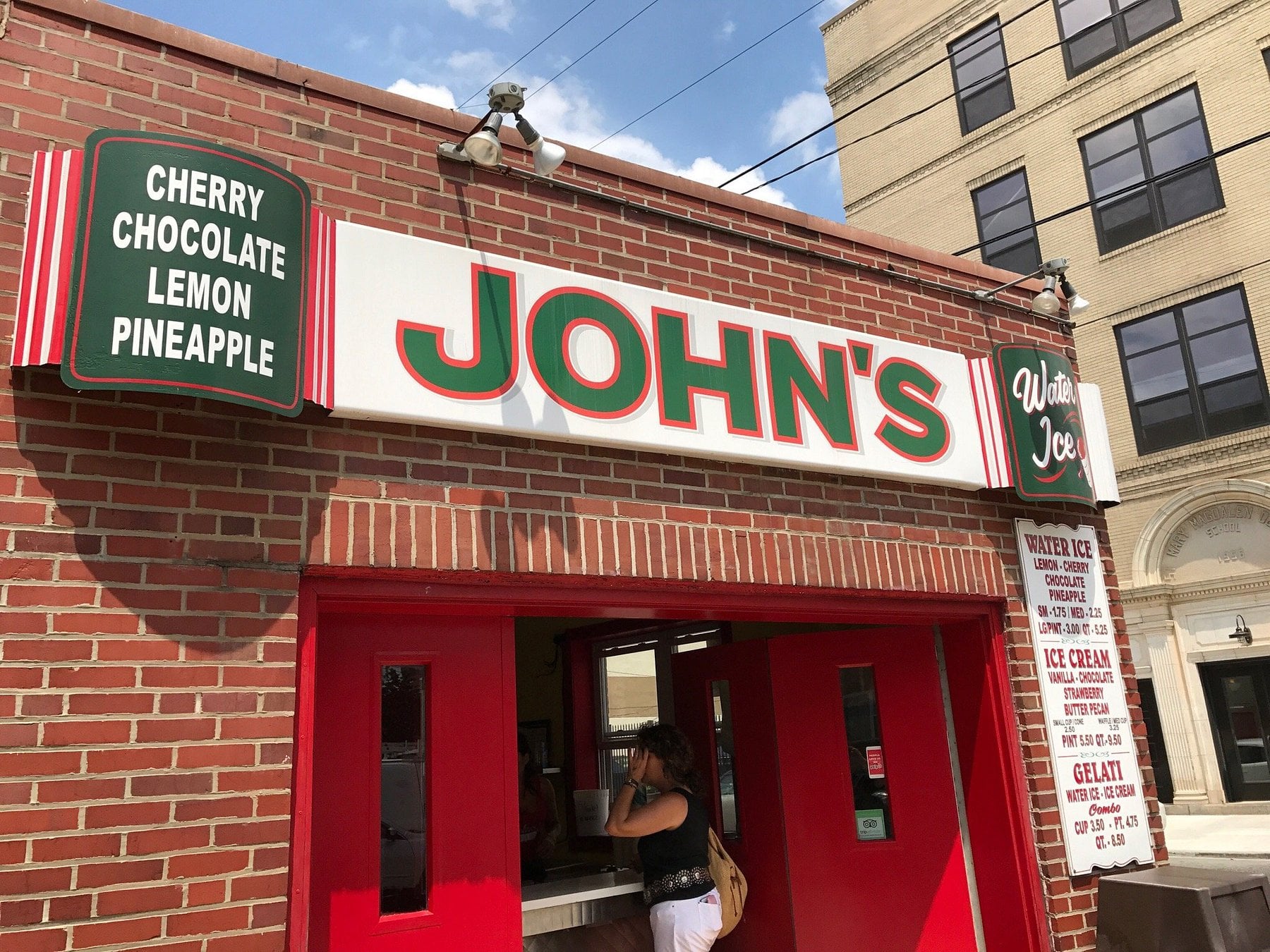 The brick storefront of John’s Water Ice, with menu boards listing flavors and prices.