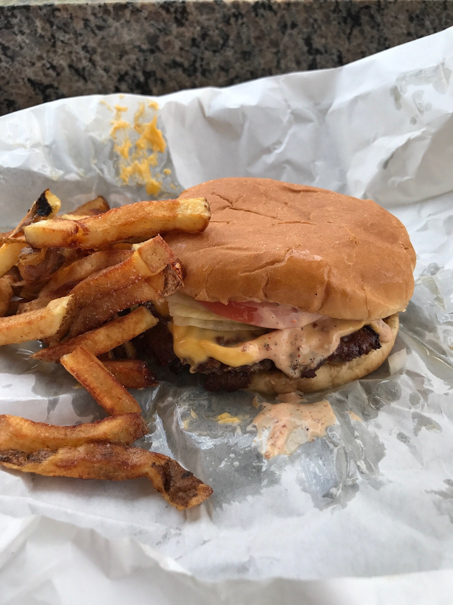 A cheeseburger with sauce and a side of french fries served on wax paper.
